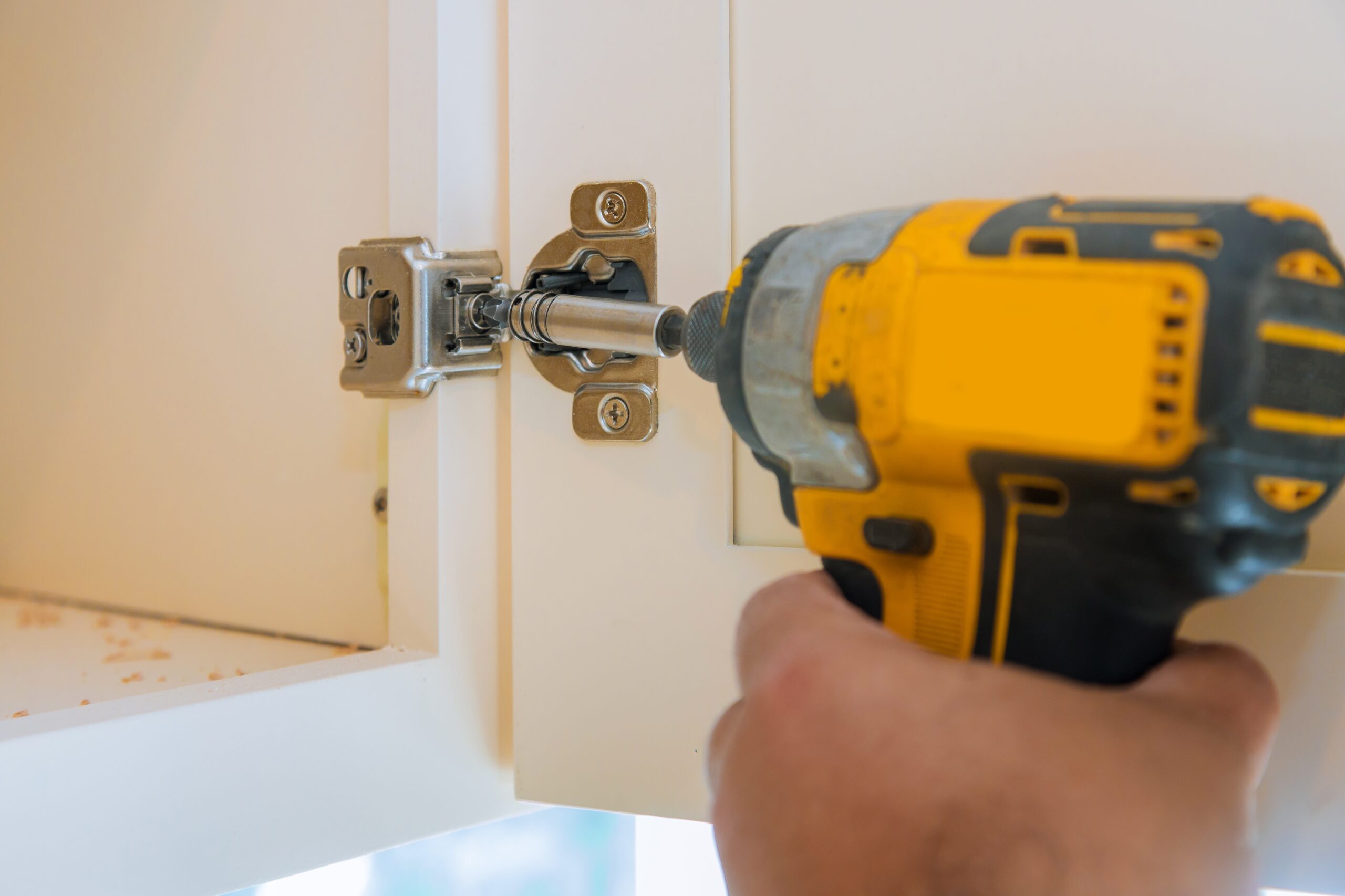 Carpentry assembly of furniture accessories in the kitchen door with hinge to a kitchen cabinet a screwdriver.